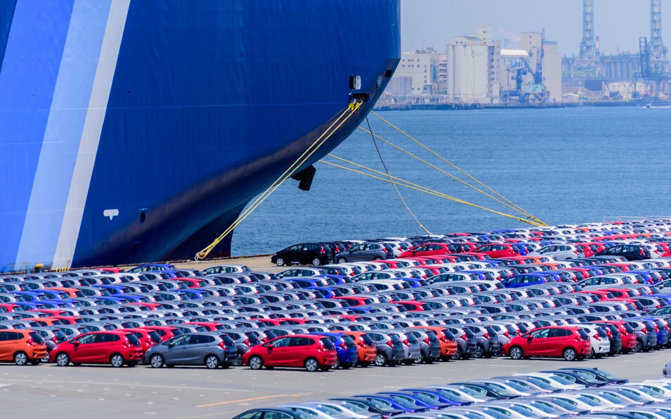 cars lined up at export terminal next to transport ship