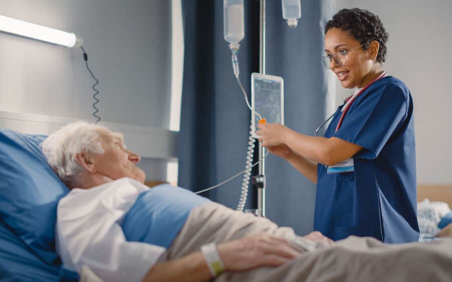 Nurse talking to patient and adjusting infusion pump IV in hospital room