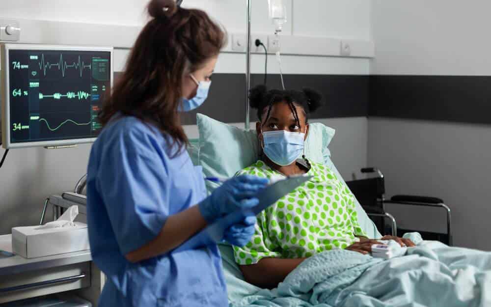 nurse speaking to young patient laying in bed in hospital room