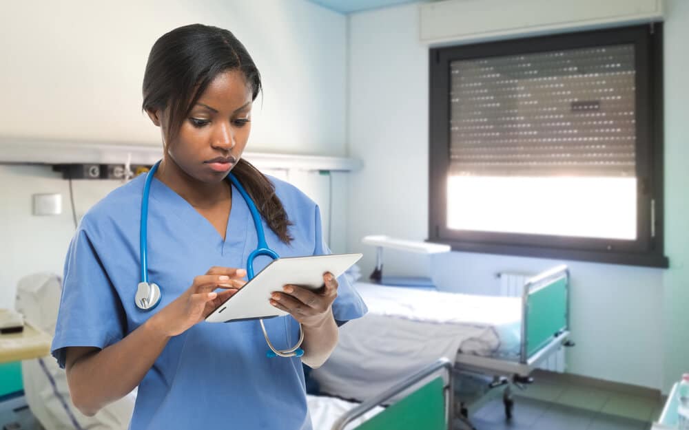 Nurse in scrubs standing in hospital room using smart tablet