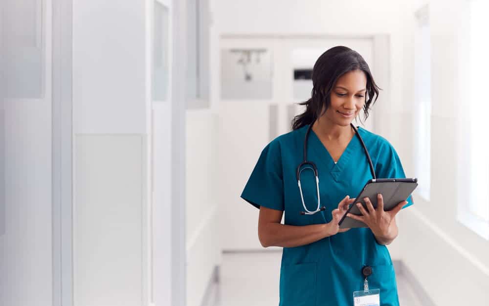 Nurse in scrubs standing in hospital hallway using tablet