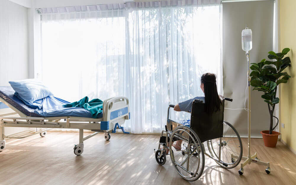 patient sitting in hospital room in wheelchair next to hospital bed