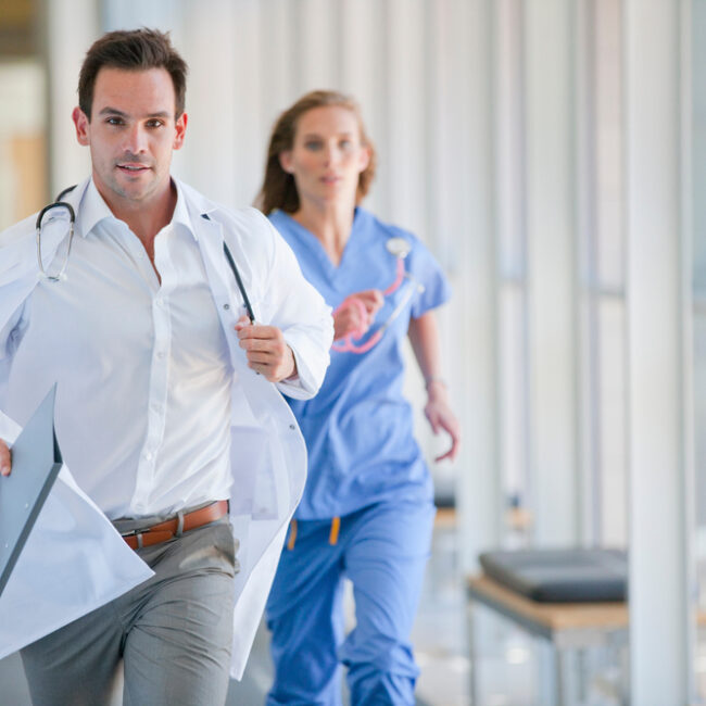 Doctor,And,Nurse,Running,Down,Hospital,Corridor,For,An,Emergency