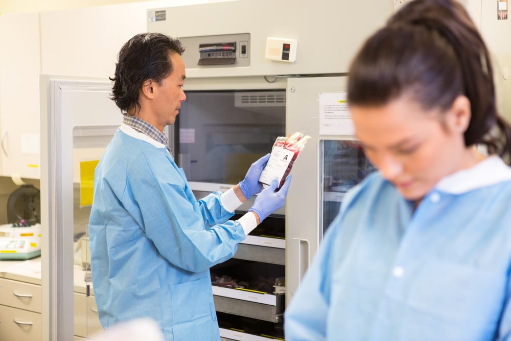 Lab workers handling blood from hospital fridge controlled by automated temperature monitoring