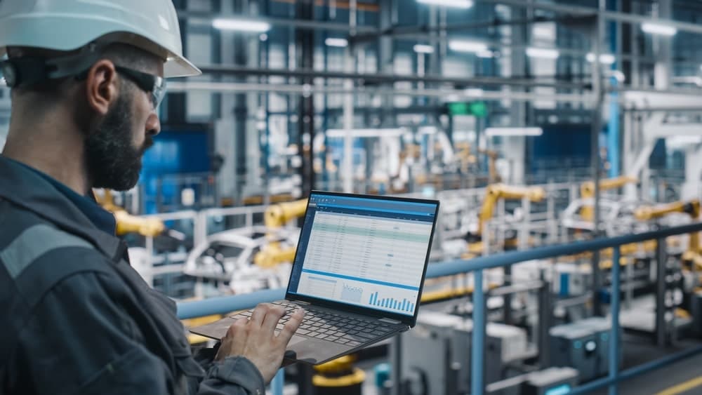 man with computer assessing vehicle location in manufacturing plant