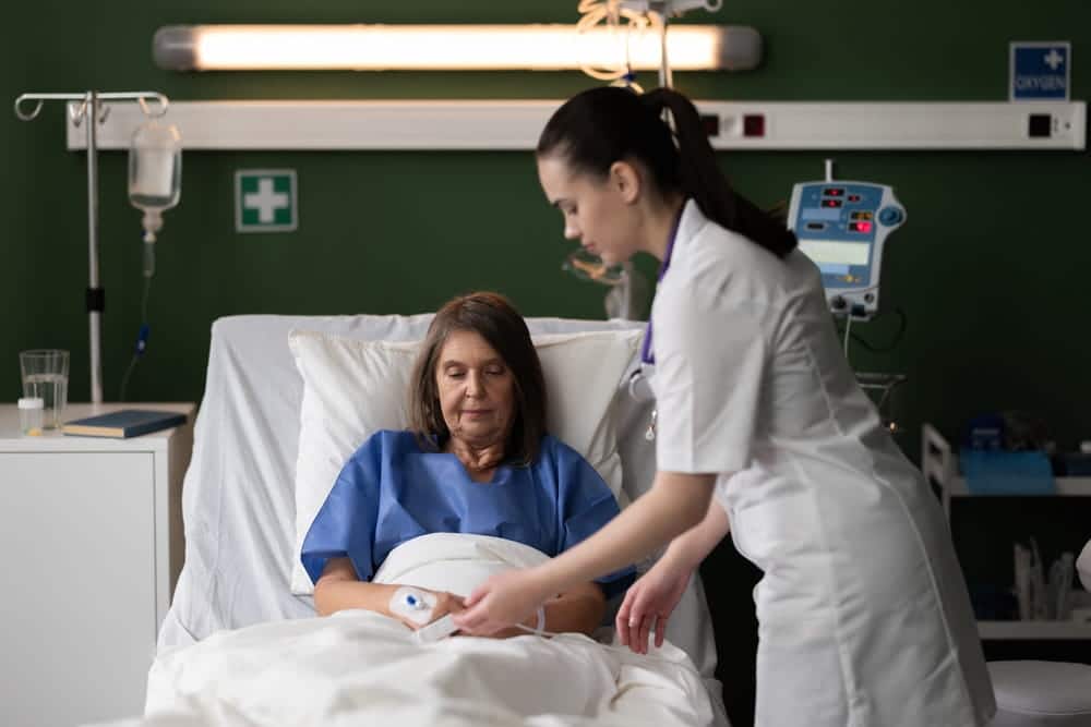 Nurse providing bedside care to a patient in a hospital room during a staff-patient encounter.